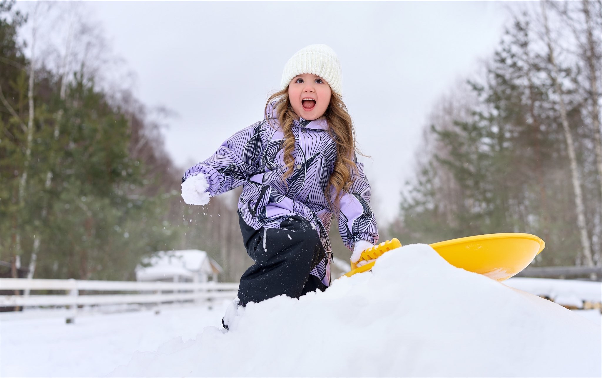 Девочка в зимнем комбинезоне лепит снежки.